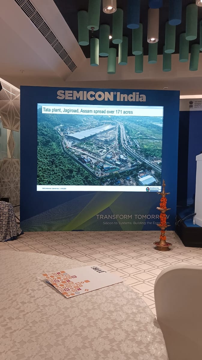 SEMICON India stage with a slide reading 'Tata plant, Jagiroad, Assam spread over 171 acres', a lit ceremonial lamp in front, and a JIBB brochure on the floor